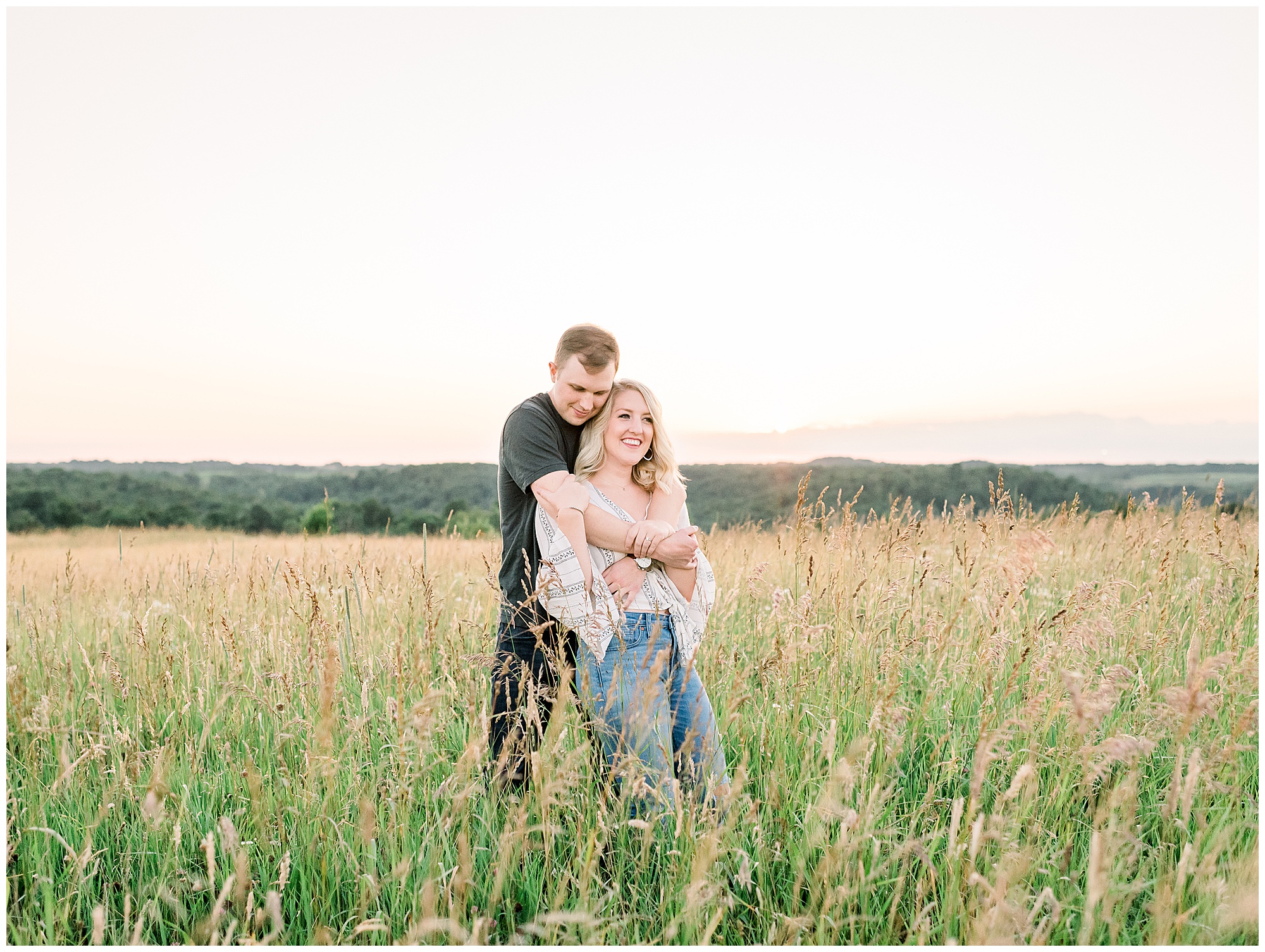 Engagement portrait of a couple in a field at sunset.